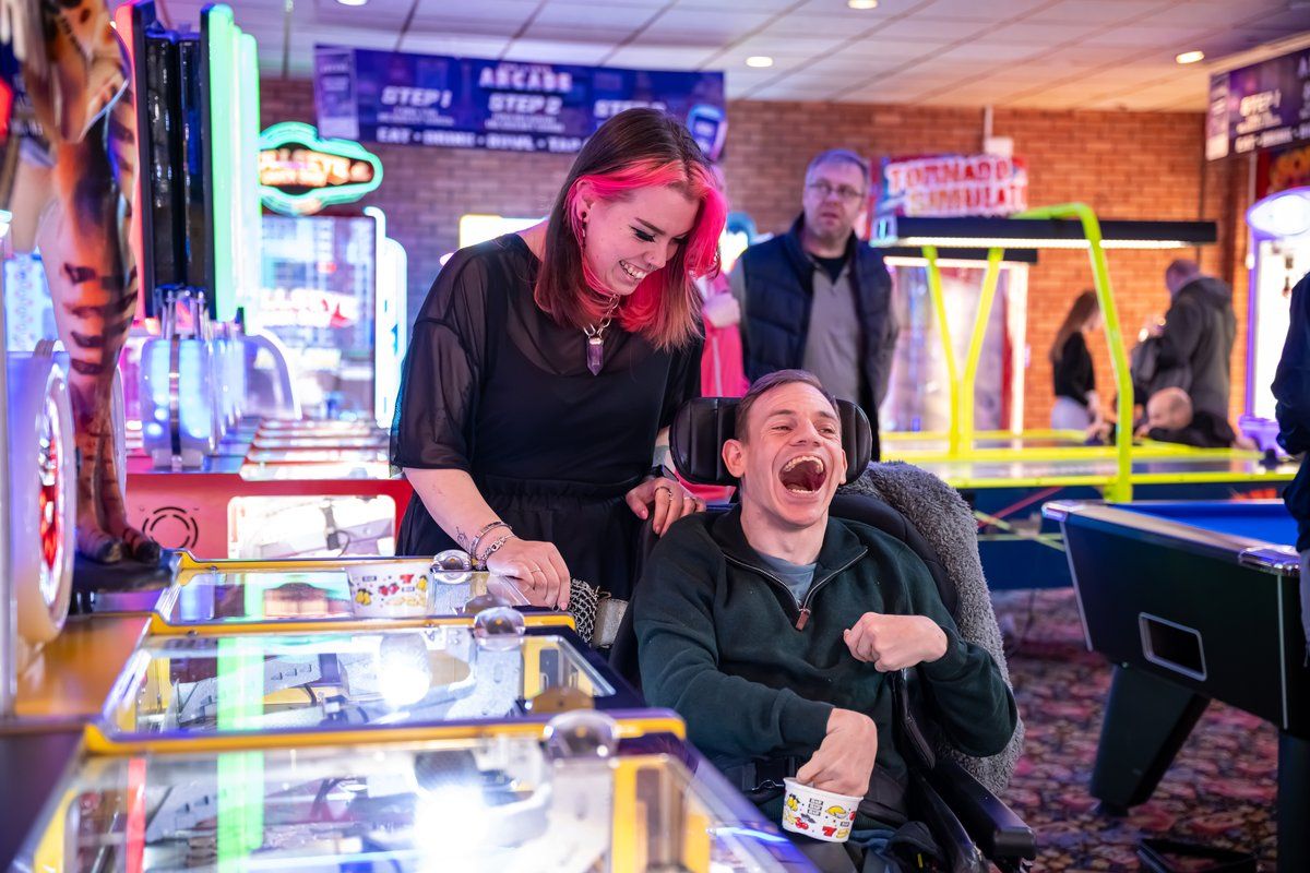 Person in a wheelchair at an arcade with a support worker, laughing