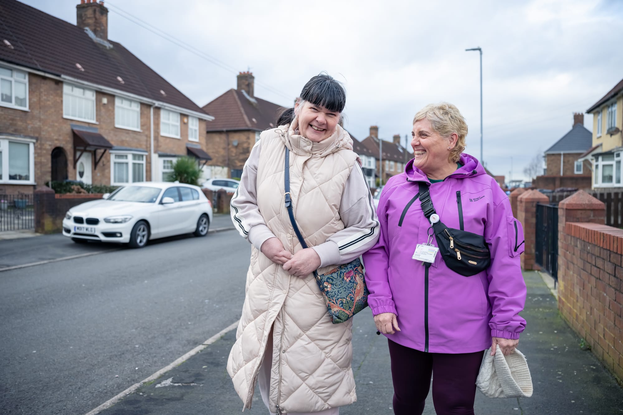A support worker and a woman supported walking outside on the pavement in a residential area, smiling